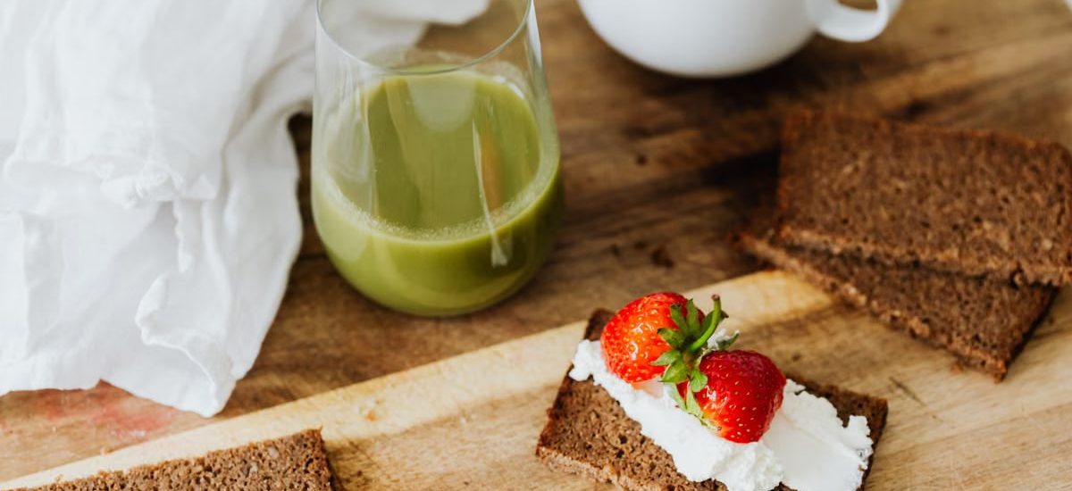 Start your day with a nutritious breakfast featuring rye toast with cream cheese and strawberries, paired with green juice and coffee.