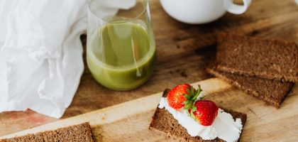 Start your day with a nutritious breakfast featuring rye toast with cream cheese and strawberries, paired with green juice and coffee.