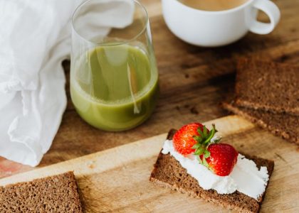 Start your day with a nutritious breakfast featuring rye toast with cream cheese and strawberries, paired with green juice and coffee.